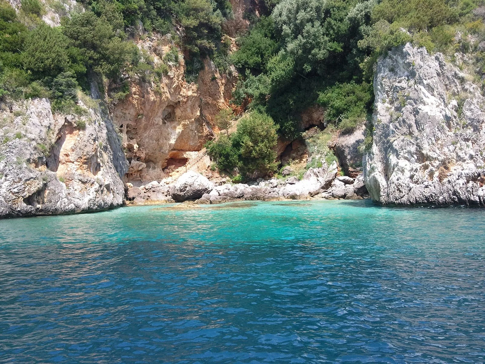 Caletta rocciosa sulla costa di Marina di Camerota con cavità carsiche nella parete di roccia, macchia mediterranea e acqua turchese