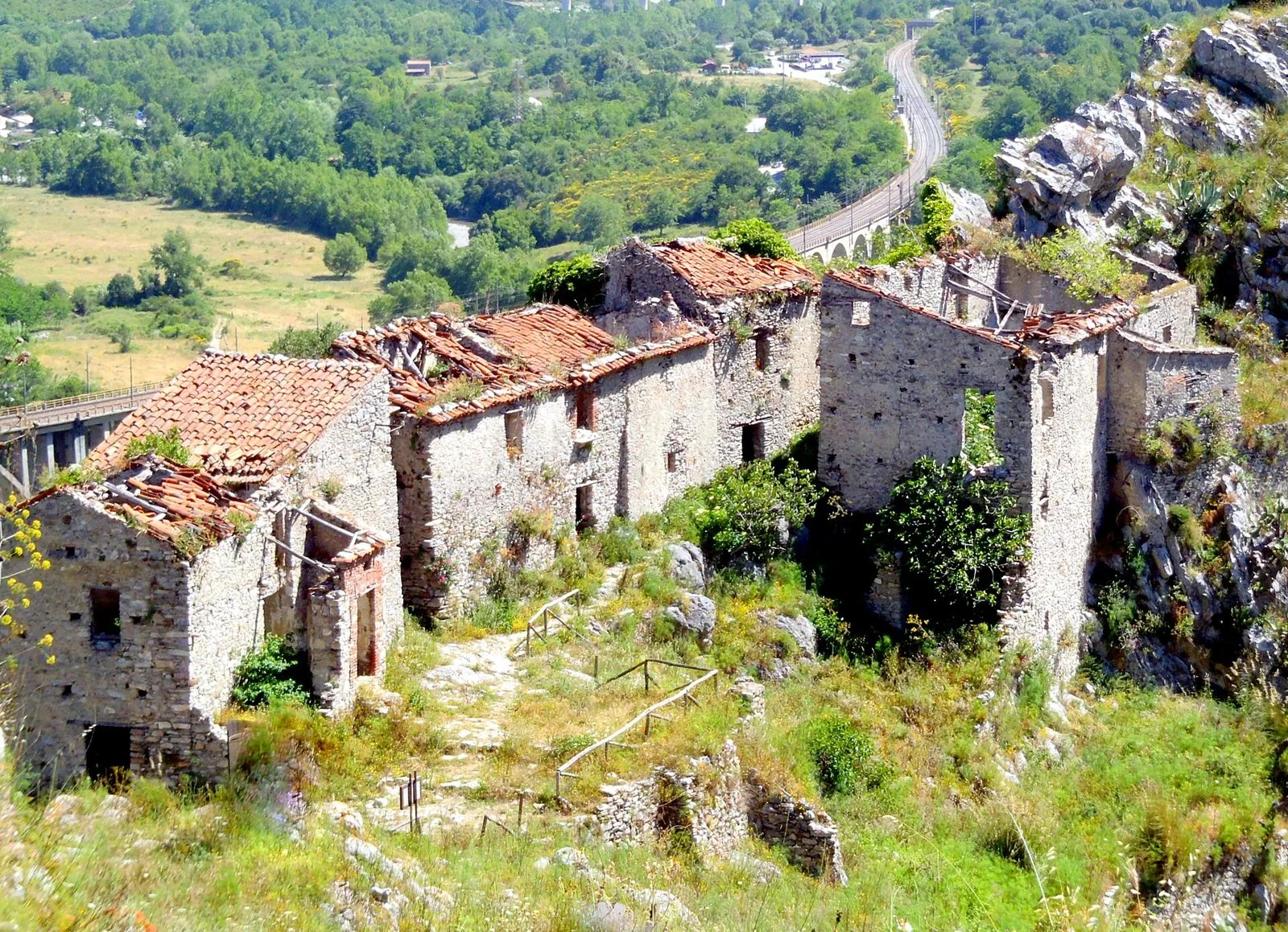 Case in pietra in rovina del borgo medievale abbandonato di San Severino di Centola, con la valle del Mingardo e il viadotto ferroviario sullo sfondo