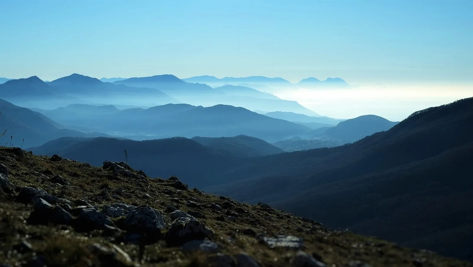 Panorama dal Monte Cervati su creste montuose in successione avvolte dalla foschia, con il golfo di Policastro in lontananza