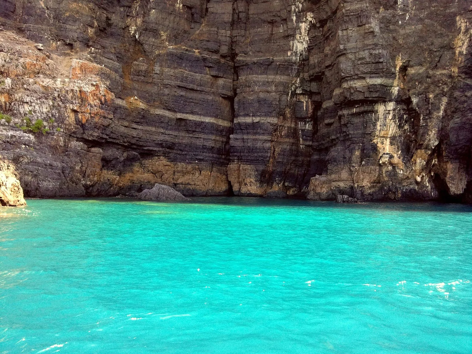 Parete rocciosa stratificata a picco sul mare color turchese lungo la Costa degli Infreschi, vista da una barca