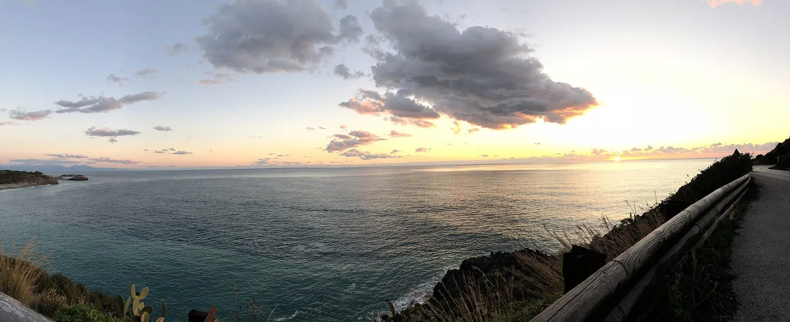 Panorama sul mare di Camerota al tramonto visto da una strada costiera con staccionata in legno e vegetazione mediterranea